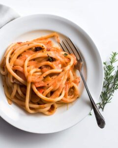 White plate with pasta in creamy tomato sauce. The sauce is smooth and orange, with hints of herbs and black pepper sprinkled over the pasta