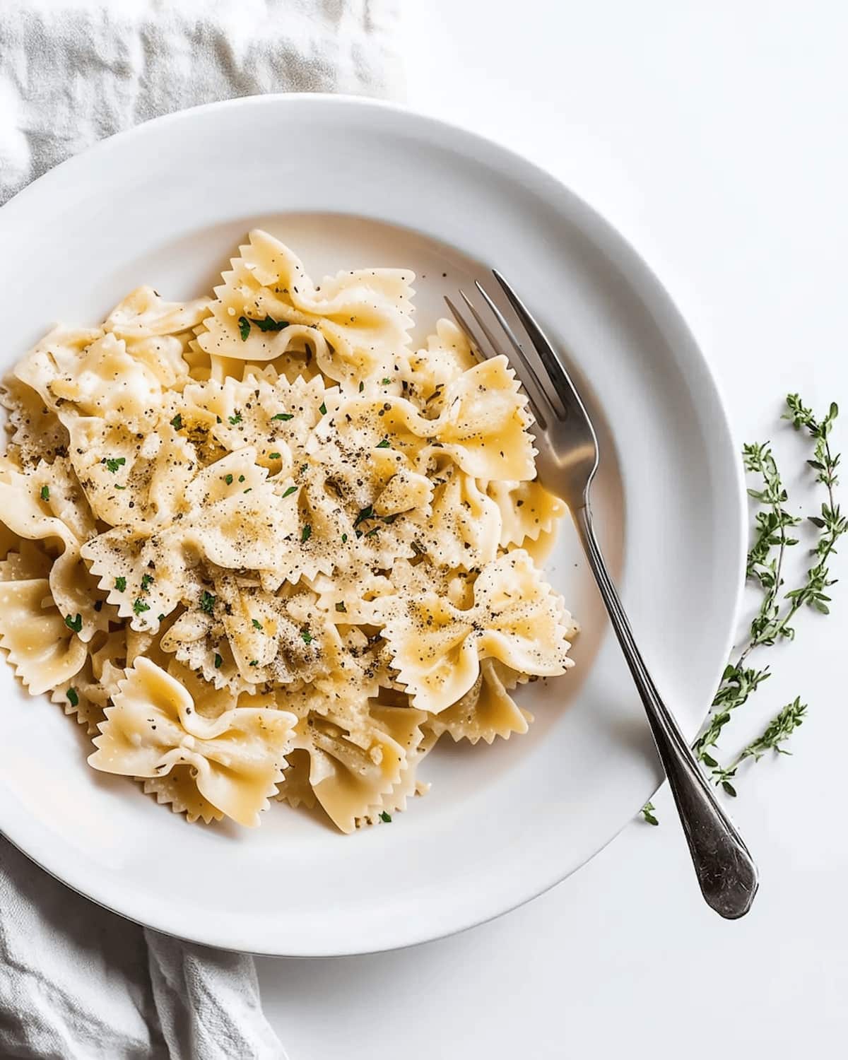 White plate with farfalle pasta coated in a creamy caramelized onion pasta sauce. The sauce is light and smooth, topped with black pepper and fresh herbs.